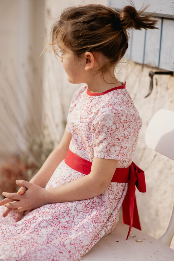 Robe enfant Castille fleurie à manches courtes portée, ceinture rouge nouée en nœud sur le côté